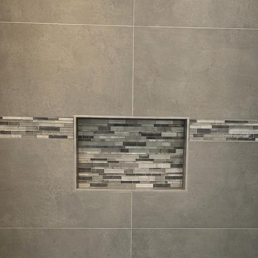 Close-up of a tiled shower wall with a mosaic band and niche